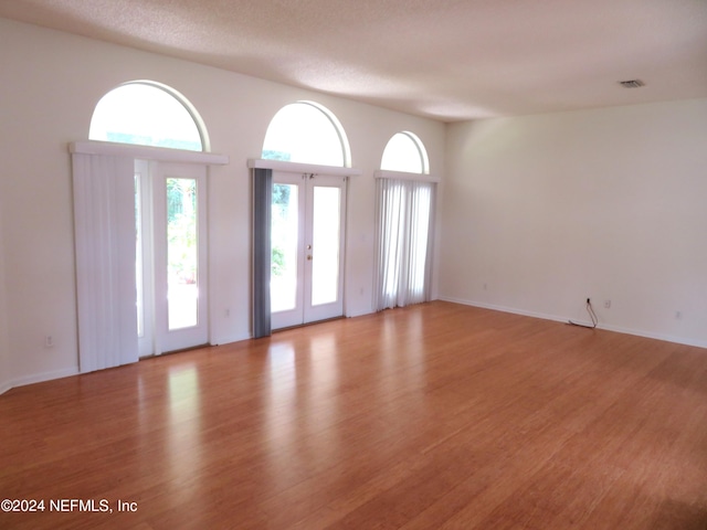 empty room with french doors, a textured ceiling, and light hardwood / wood-style flooring