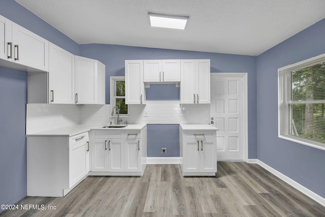 kitchen with sink, light wood-type flooring, white cabinetry, and tasteful backsplash