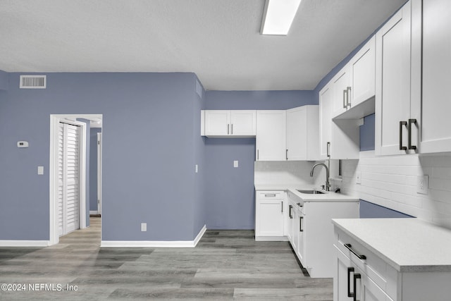 kitchen with a textured ceiling, sink, light wood-type flooring, and white cabinets