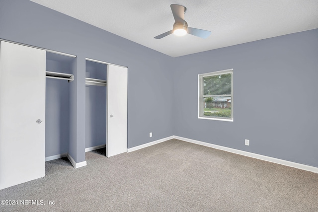 unfurnished bedroom featuring carpet flooring, ceiling fan, and multiple closets