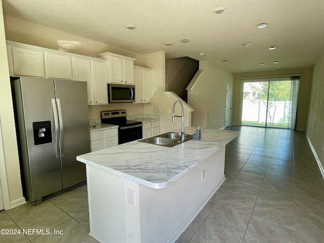 kitchen featuring white cabinets, light tile patterned floors, stainless steel appliances, sink, and a center island with sink