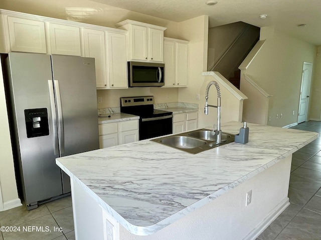 kitchen with white cabinetry, sink, appliances with stainless steel finishes, a center island with sink, and light tile patterned flooring