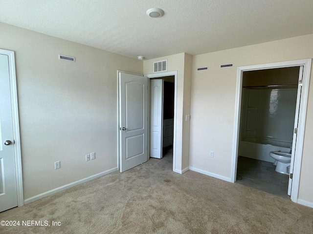 unfurnished bedroom featuring a textured ceiling, light carpet, and ensuite bath