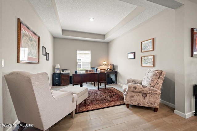 office space with a textured ceiling, light wood-type flooring, and a tray ceiling