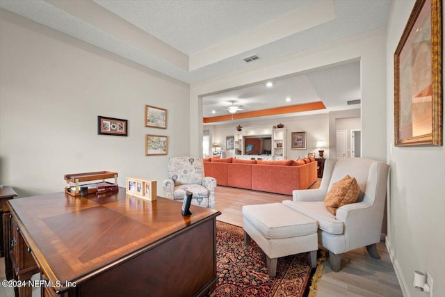 living room featuring hardwood / wood-style floors, a tray ceiling, a textured ceiling, and ceiling fan