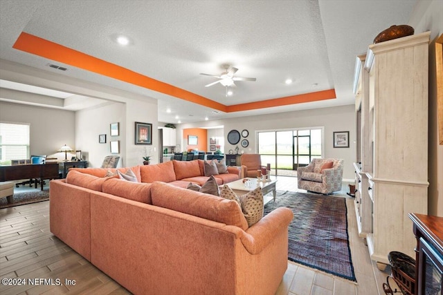 living room featuring a tray ceiling, ceiling fan, light hardwood / wood-style floors, and a textured ceiling