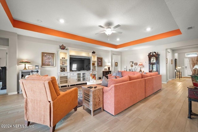 living room featuring light wood-type flooring, a raised ceiling, a textured ceiling, and ceiling fan