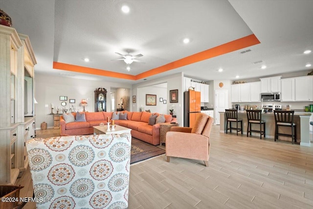 living room featuring ceiling fan, a tray ceiling, and light hardwood / wood-style floors