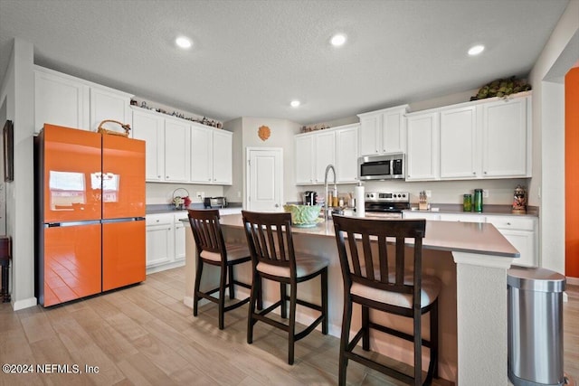 kitchen with white cabinets, light wood-type flooring, appliances with stainless steel finishes, an island with sink, and a breakfast bar