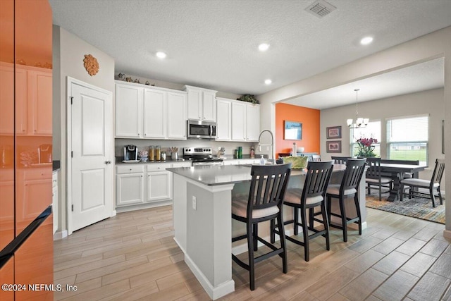 kitchen featuring a center island with sink, light hardwood / wood-style flooring, stainless steel appliances, and white cabinets