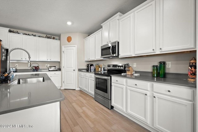 kitchen featuring a textured ceiling, stainless steel appliances, sink, white cabinets, and light hardwood / wood-style floors