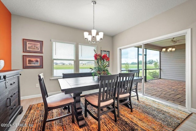 dining area with hardwood / wood-style floors, ceiling fan with notable chandelier, and a textured ceiling