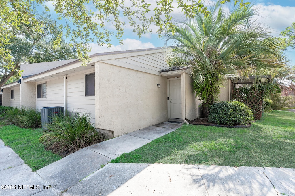 view of property exterior featuring central air condition unit, stucco siding, and a yard