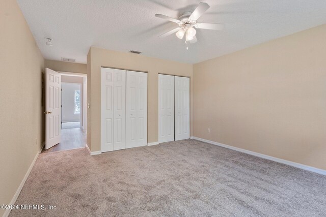 unfurnished bedroom with two closets, ceiling fan, light carpet, and a textured ceiling