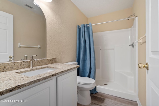 bathroom with hardwood / wood-style floors, walk in shower, toilet, vanity, and a textured ceiling