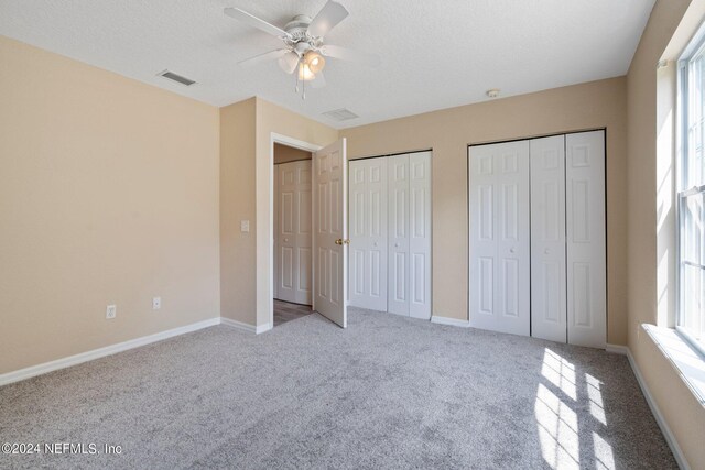 unfurnished bedroom with light carpet, multiple windows, multiple closets, and ceiling fan