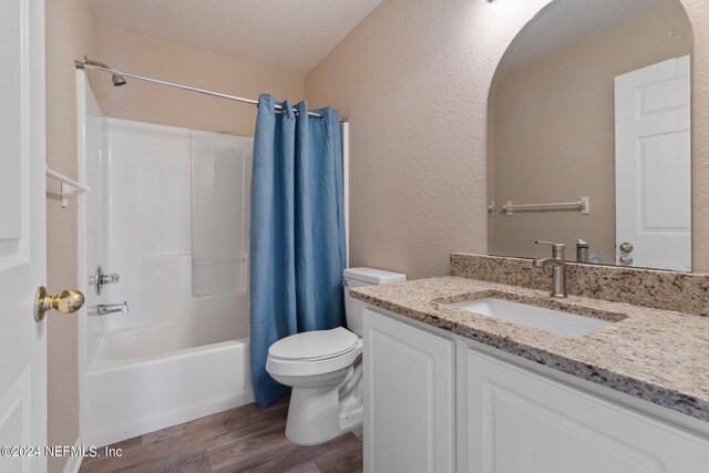 full bathroom with hardwood / wood-style flooring, shower / bathtub combination with curtain, toilet, vanity, and a textured ceiling