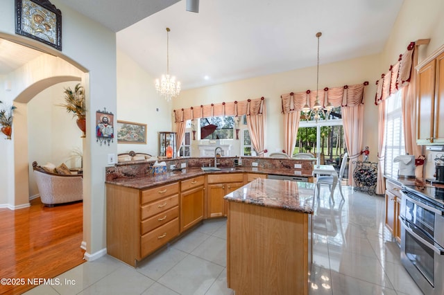 kitchen with dark stone counters, range with two ovens, arched walkways, a notable chandelier, and a sink