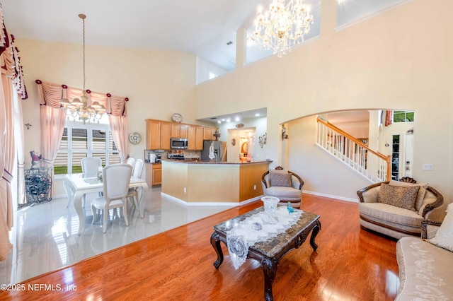 living area with a notable chandelier, light wood-style flooring, arched walkways, a towering ceiling, and stairs