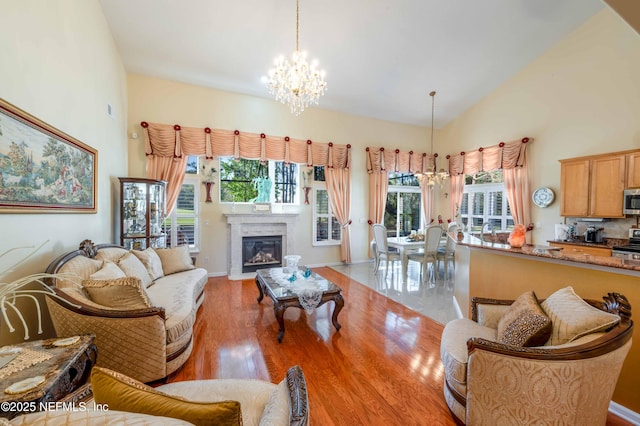 living room with high vaulted ceiling, light wood-style flooring, a glass covered fireplace, an inviting chandelier, and baseboards