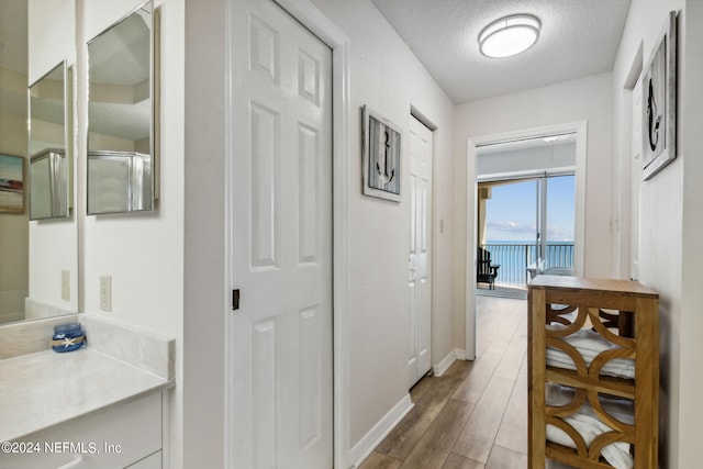 hallway featuring a textured ceiling, a water view, and light hardwood / wood-style floors