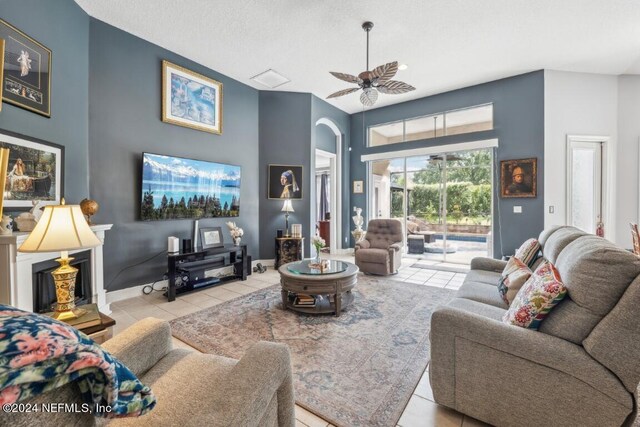 tiled living room with a textured ceiling, ceiling fan, and a fireplace