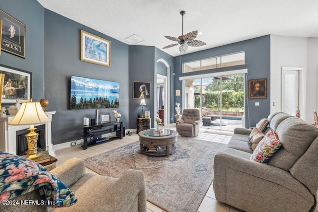 tiled living room featuring arched walkways, a ceiling fan, and baseboards