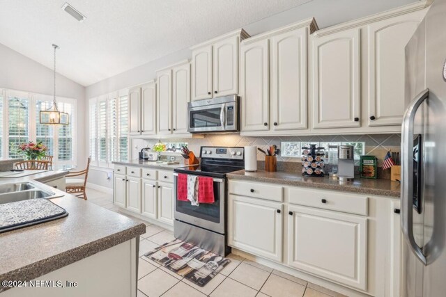 kitchen featuring backsplash, light tile patterned floors, hanging light fixtures, appliances with stainless steel finishes, and lofted ceiling