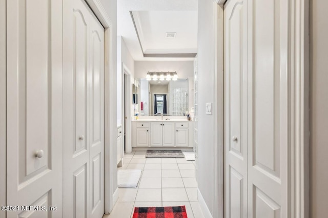 hall featuring light tile patterned floors, a raised ceiling, and sink