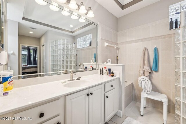 bathroom with vanity, a raised ceiling, tiled shower, tile walls, and tile patterned flooring