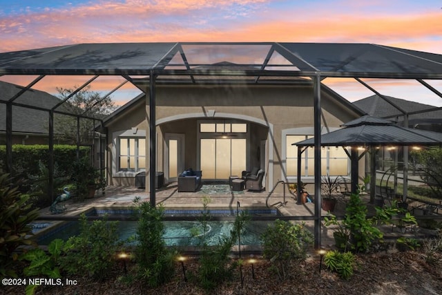 back house at dusk featuring glass enclosure and a patio area