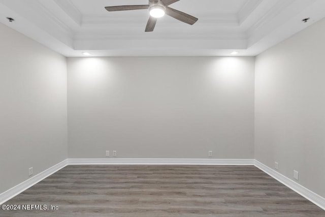 empty room with a tray ceiling, ceiling fan, wood-type flooring, and ornamental molding