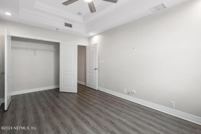 unfurnished bedroom with a raised ceiling, a closet, crown molding, dark wood-type flooring, and ceiling fan