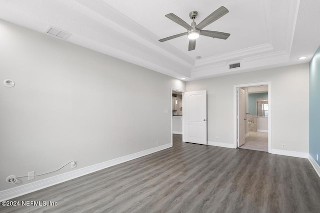 unfurnished bedroom featuring hardwood / wood-style flooring, ensuite bathroom, a tray ceiling, ceiling fan, and ornamental molding