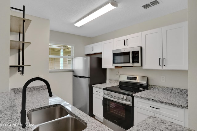 kitchen with white cabinets, sink, a textured ceiling, appliances with stainless steel finishes, and light stone countertops