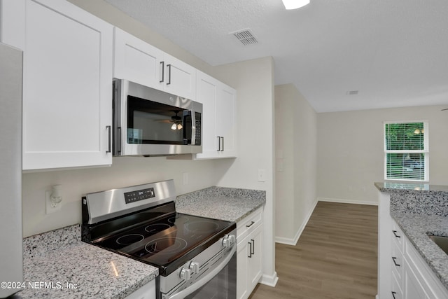 kitchen with light stone countertops, stainless steel appliances, hardwood / wood-style floors, and white cabinetry