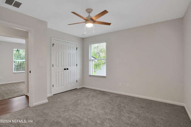 unfurnished bedroom featuring a closet, ceiling fan, multiple windows, and carpet flooring