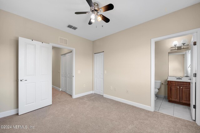 unfurnished bedroom featuring light carpet, ensuite bath, sink, ceiling fan, and a closet