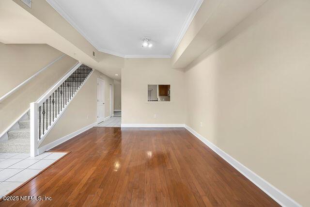 unfurnished living room featuring crown molding, stairs, wood-type flooring, and baseboards