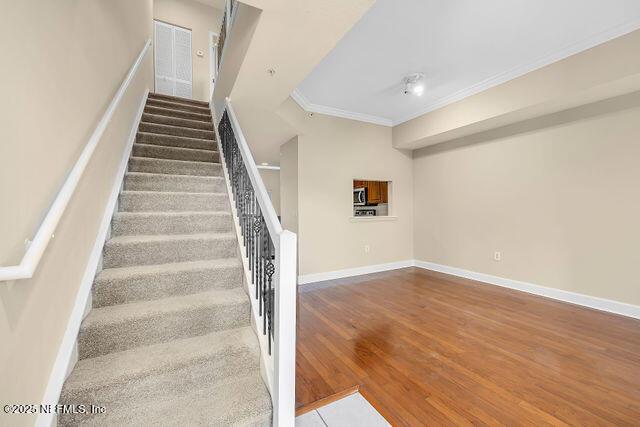 staircase featuring crown molding, wood finished floors, and baseboards