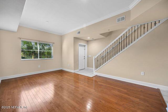 unfurnished living room with wood-type flooring, crown molding, baseboards, and stairway