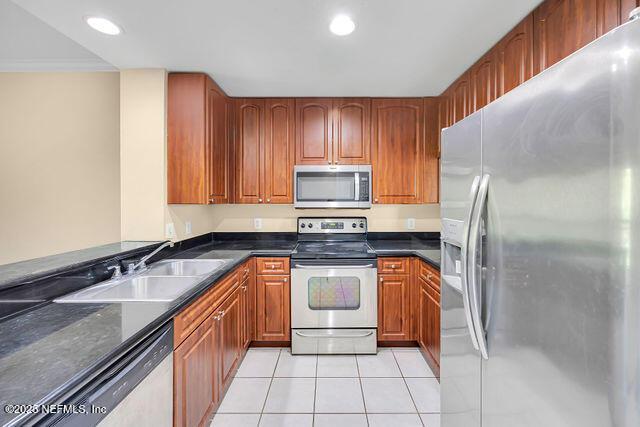 kitchen featuring stainless steel appliances, a sink, light tile patterned floors, brown cabinetry, and recessed lighting