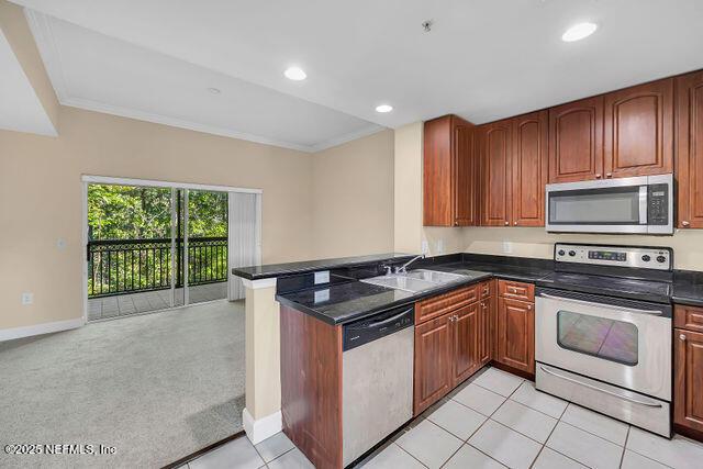 kitchen featuring stainless steel appliances, a peninsula, a sink, dark countertops, and baseboards