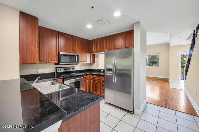 kitchen featuring stainless steel appliances, a sink, light tile patterned floors, baseboards, and dark stone counters