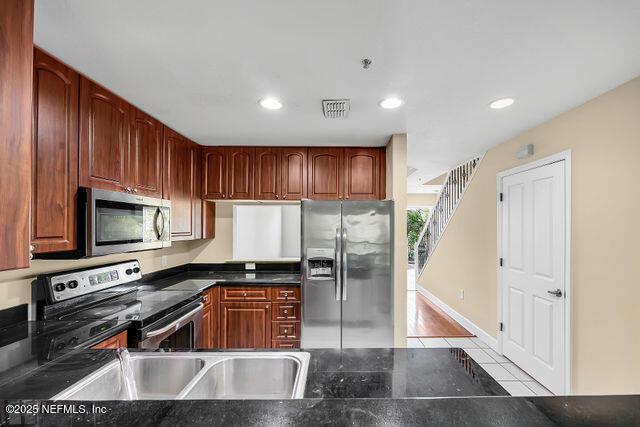 kitchen with stainless steel appliances, light tile patterned floors, dark countertops, recessed lighting, and a sink
