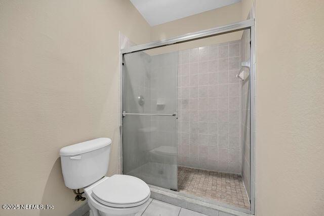 full bath with a stall shower, toilet, and tile patterned flooring