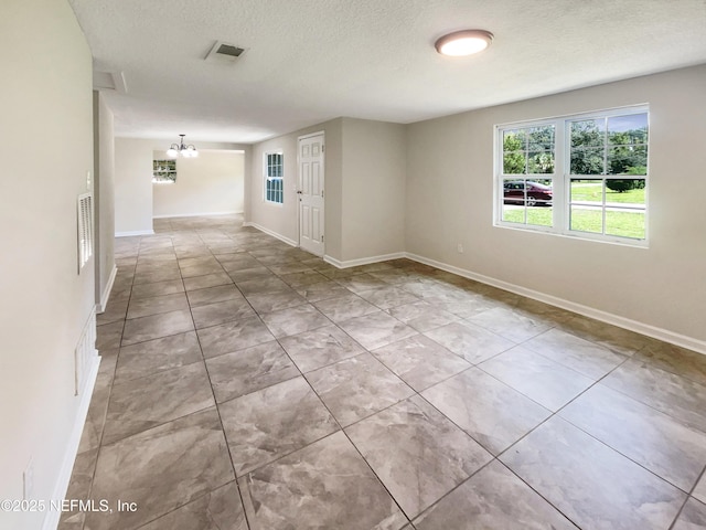 spare room with baseboards, a notable chandelier, visible vents, and a textured ceiling