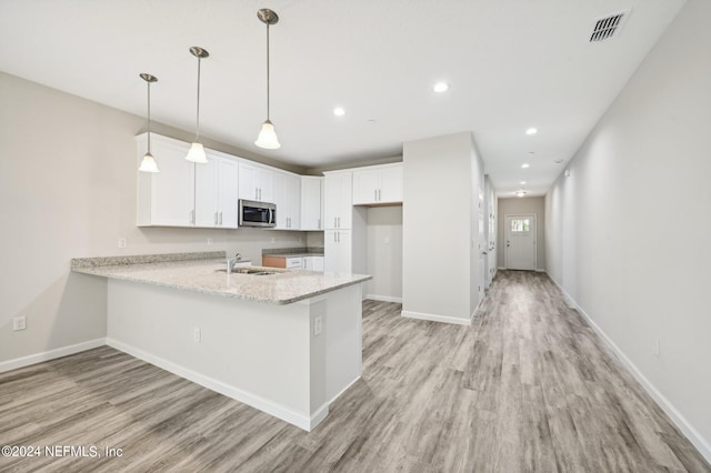 kitchen with pendant lighting, white cabinets, sink, light hardwood / wood-style floors, and kitchen peninsula