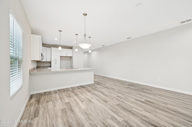 kitchen with light stone counters, kitchen peninsula, pendant lighting, light hardwood / wood-style floors, and white cabinets