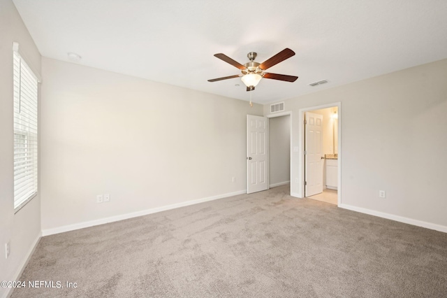 interior space featuring connected bathroom, multiple windows, ceiling fan, and light colored carpet